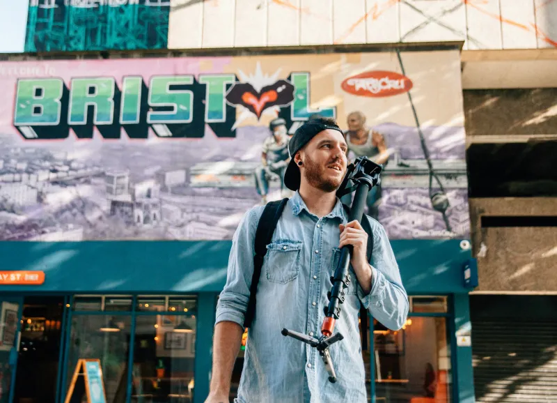 man holding camera tripod standing near store